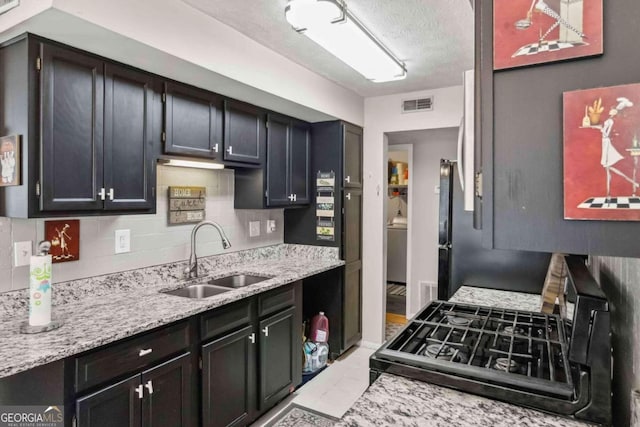 kitchen with black range, sink, light stone countertops, a textured ceiling, and tasteful backsplash