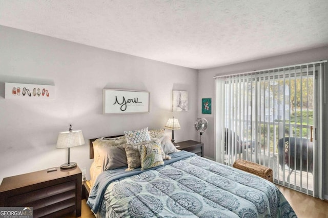 bedroom featuring access to exterior, hardwood / wood-style floors, and a textured ceiling