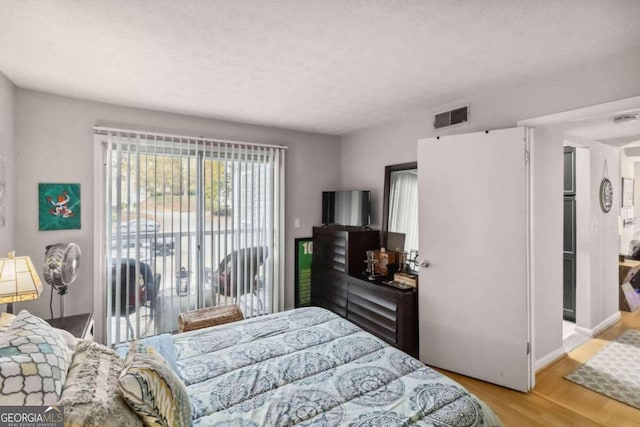 bedroom with access to exterior, light hardwood / wood-style flooring, and a textured ceiling