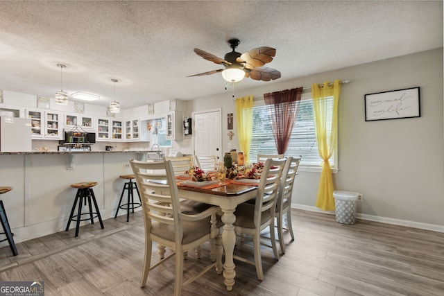 dining area with a textured ceiling, light wood-type flooring, and ceiling fan