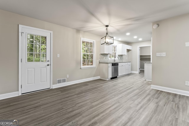 kitchen with a wealth of natural light, white cabinetry, hanging light fixtures, and stainless steel dishwasher