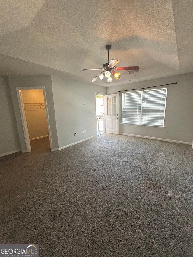 interior space featuring dark colored carpet, ceiling fan, a spacious closet, a textured ceiling, and a closet