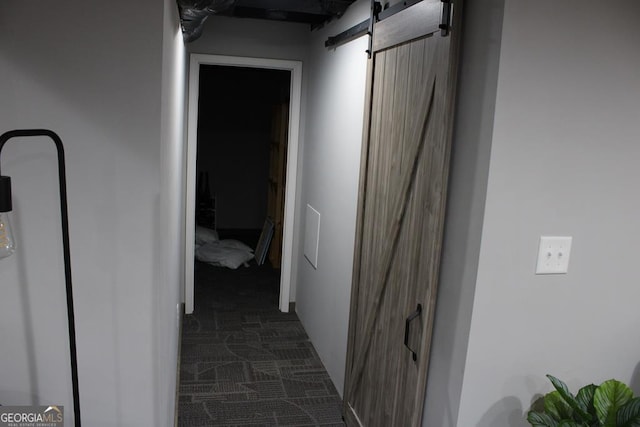 hallway featuring dark colored carpet and a barn door