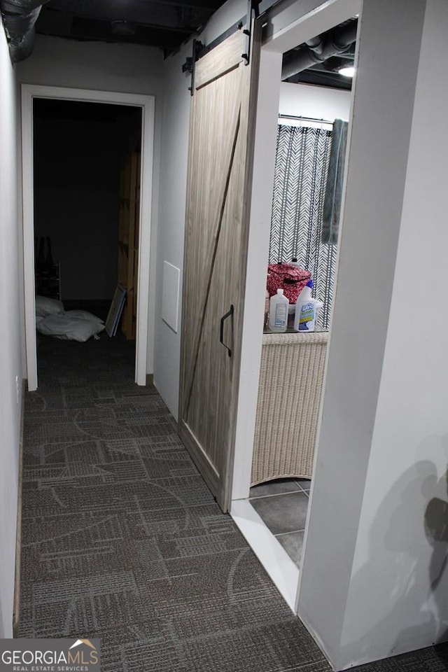 corridor featuring a barn door and dark colored carpet