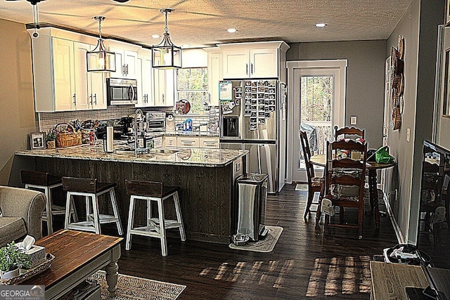 kitchen with light stone countertops, appliances with stainless steel finishes, a textured ceiling, pendant lighting, and white cabinets