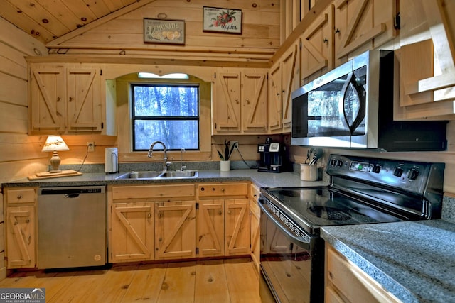 kitchen featuring appliances with stainless steel finishes, light wood-type flooring, vaulted ceiling, sink, and wood walls