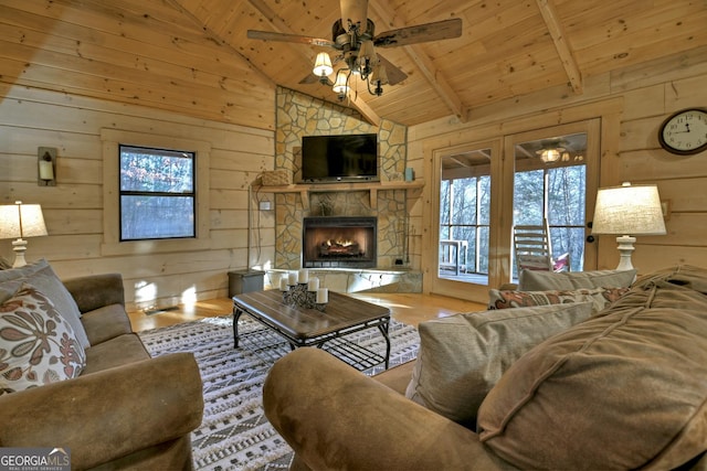 living room featuring wood walls, wooden ceiling, a stone fireplace, ceiling fan, and beamed ceiling