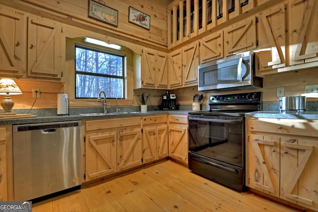 kitchen featuring appliances with stainless steel finishes, light brown cabinetry, wooden walls, sink, and light hardwood / wood-style floors