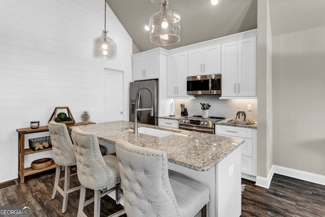 kitchen featuring white cabinetry, appliances with stainless steel finishes, a kitchen island with sink, decorative light fixtures, and light stone countertops