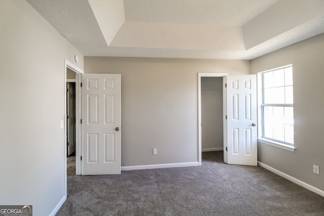 unfurnished bedroom featuring dark carpet, a textured ceiling, and multiple windows