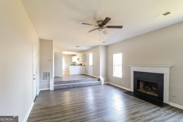 unfurnished living room with a textured ceiling, ceiling fan, and dark wood-type flooring