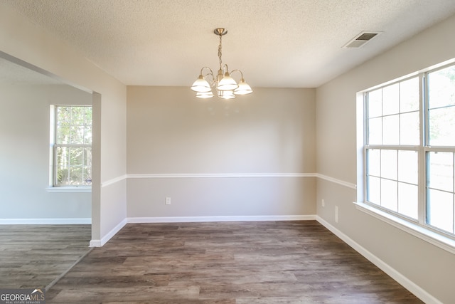 spare room with a textured ceiling, a notable chandelier, and dark wood-type flooring