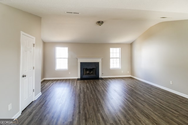 unfurnished living room with a textured ceiling, dark wood-type flooring, a wealth of natural light, and vaulted ceiling