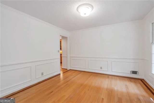 empty room featuring a textured ceiling, light hardwood / wood-style floors, and crown molding