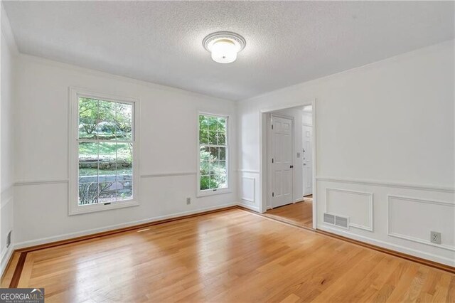 spare room featuring plenty of natural light, a textured ceiling, and light wood-type flooring