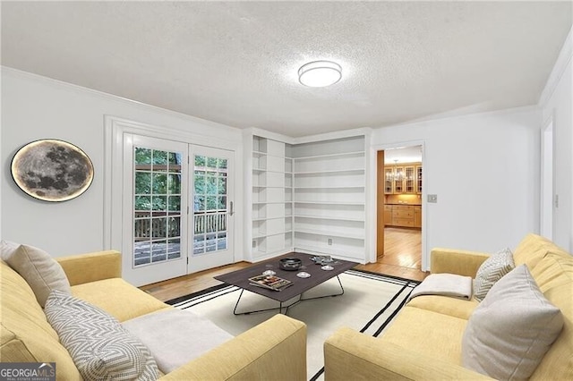 living room with built in features, light wood-type flooring, a textured ceiling, and ornamental molding