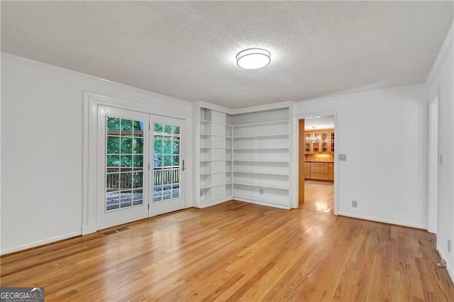 unfurnished room with built in features, ornamental molding, a textured ceiling, and light wood-type flooring