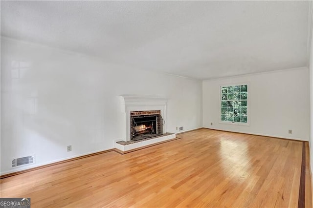 unfurnished living room featuring a brick fireplace and light wood-type flooring