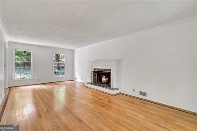 unfurnished living room with a textured ceiling, light wood-type flooring, and crown molding