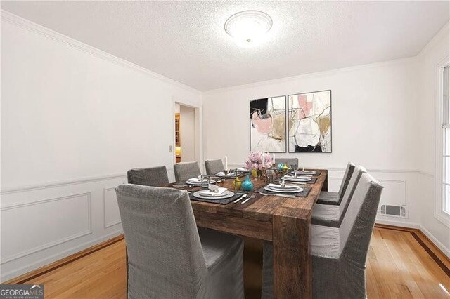 dining area featuring light hardwood / wood-style flooring, a textured ceiling, and ornamental molding