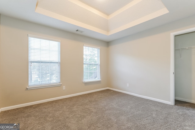 unfurnished bedroom featuring carpet, a tray ceiling, and a closet