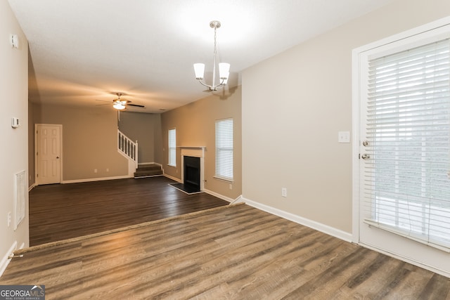 unfurnished living room with a wealth of natural light, dark hardwood / wood-style flooring, and ceiling fan with notable chandelier