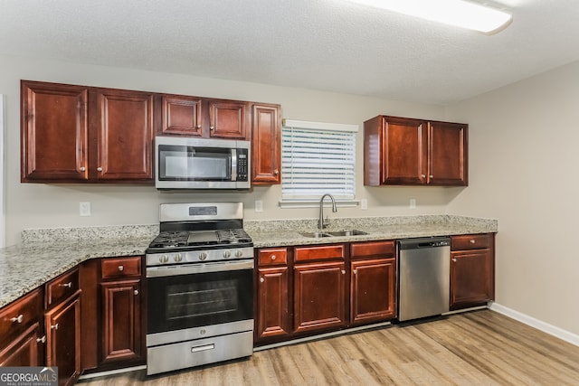 kitchen with light stone countertops, sink, light wood-type flooring, and stainless steel appliances