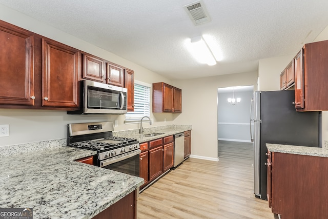 kitchen featuring light stone countertops, appliances with stainless steel finishes, light wood-type flooring, a textured ceiling, and sink