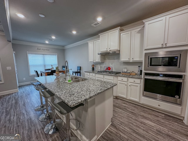 kitchen with a kitchen island with sink, sink, ornamental molding, appliances with stainless steel finishes, and white cabinetry