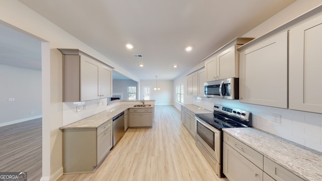 kitchen featuring light hardwood / wood-style flooring, gray cabinets, appliances with stainless steel finishes, light stone counters, and a breakfast bar area