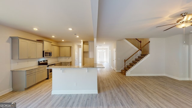 kitchen with light stone countertops, ceiling fan, light hardwood / wood-style floors, a breakfast bar, and appliances with stainless steel finishes