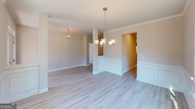 empty room with an inviting chandelier, light hardwood / wood-style flooring, and ornamental molding