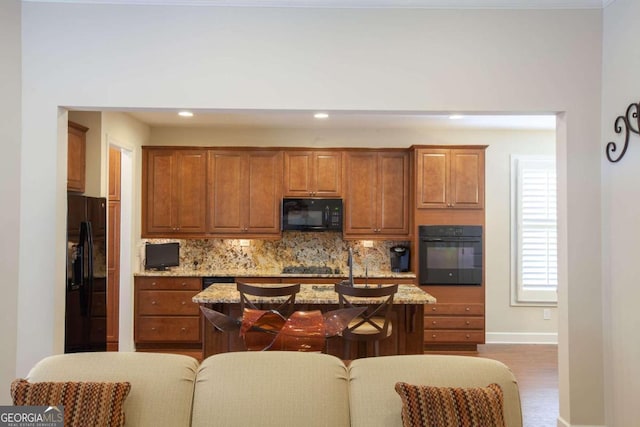 kitchen featuring light stone countertops, tasteful backsplash, dark hardwood / wood-style flooring, a center island with sink, and black appliances