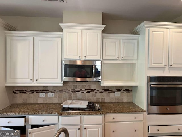 kitchen featuring white cabinets, backsplash, stainless steel appliances, and dark stone counters