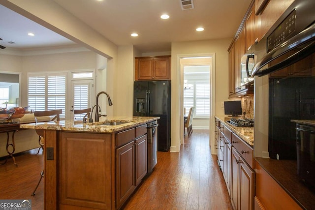 kitchen with sink, hardwood / wood-style floors, a breakfast bar area, a center island with sink, and black appliances