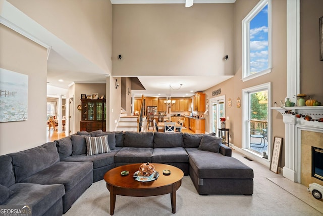 carpeted living room featuring a towering ceiling, a notable chandelier, and a premium fireplace