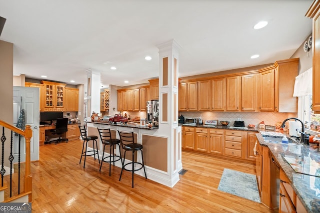 kitchen with a kitchen bar, light hardwood / wood-style floors, dark stone countertops, and sink