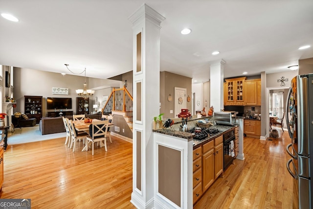 kitchen with stainless steel fridge, light hardwood / wood-style flooring, a notable chandelier, dark stone countertops, and oven