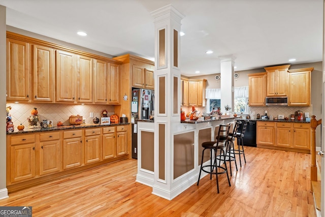 kitchen with appliances with stainless steel finishes, tasteful backsplash, light hardwood / wood-style floors, a breakfast bar area, and decorative columns