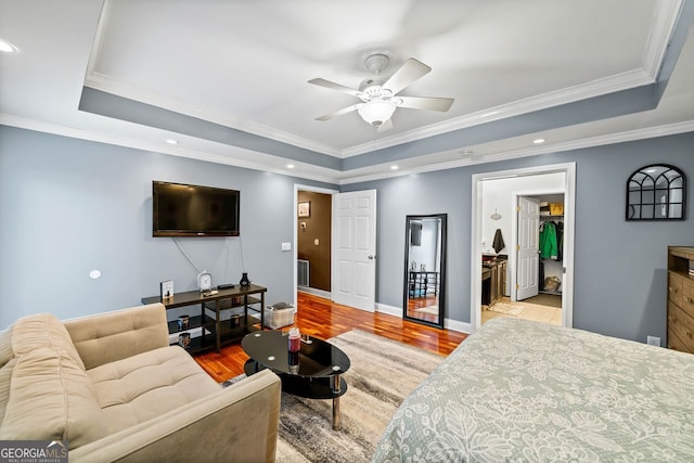 bedroom featuring light hardwood / wood-style floors, ceiling fan, ornamental molding, and a tray ceiling