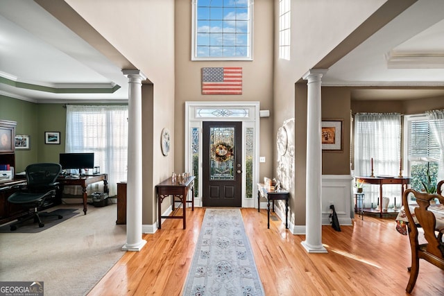 foyer with light hardwood / wood-style floors, decorative columns, crown molding, and a tray ceiling