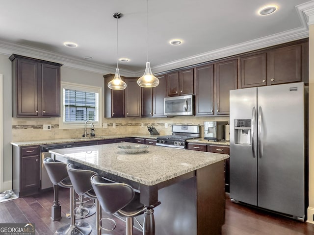 kitchen with stainless steel appliances, dark wood-type flooring, a sink, a center island, and decorative light fixtures