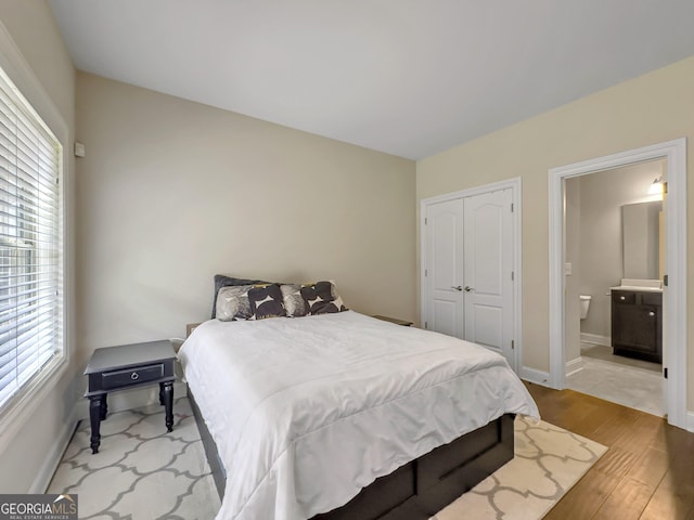 bedroom featuring a closet, light wood-style flooring, baseboards, and ensuite bathroom