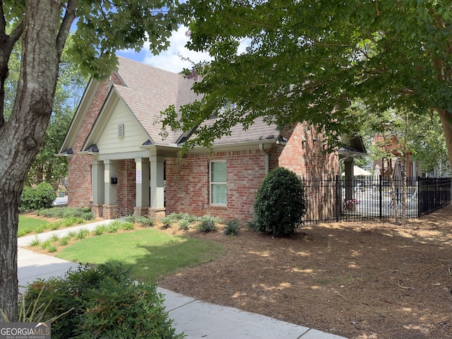 view of front of property with brick siding, roof with shingles, a front lawn, and fence