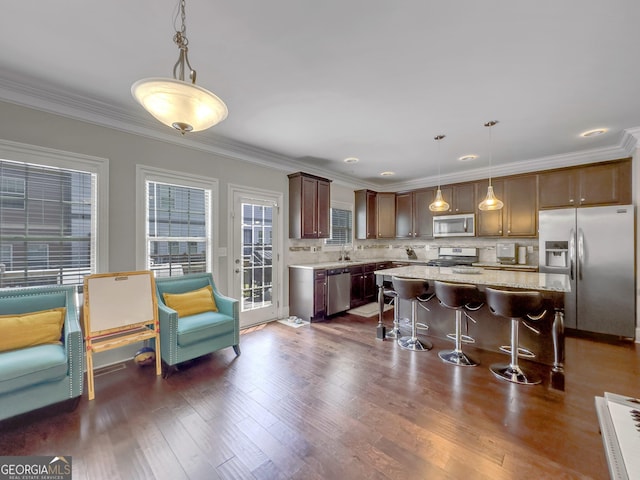 kitchen with dark wood-style floors, hanging light fixtures, appliances with stainless steel finishes, a kitchen island, and a kitchen breakfast bar