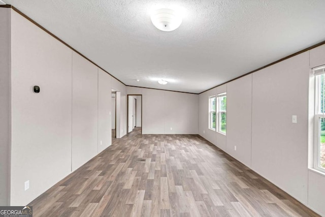 empty room with light hardwood / wood-style floors, a textured ceiling, and ornamental molding