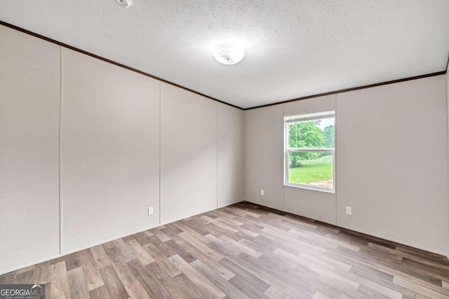 empty room featuring a textured ceiling, light hardwood / wood-style flooring, and ornamental molding