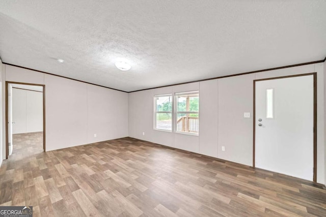 empty room with a textured ceiling, light hardwood / wood-style floors, and crown molding