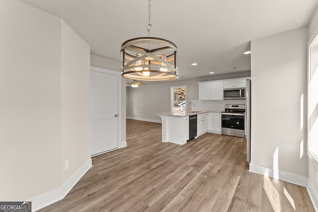 kitchen with hanging light fixtures, kitchen peninsula, appliances with stainless steel finishes, white cabinets, and light wood-type flooring