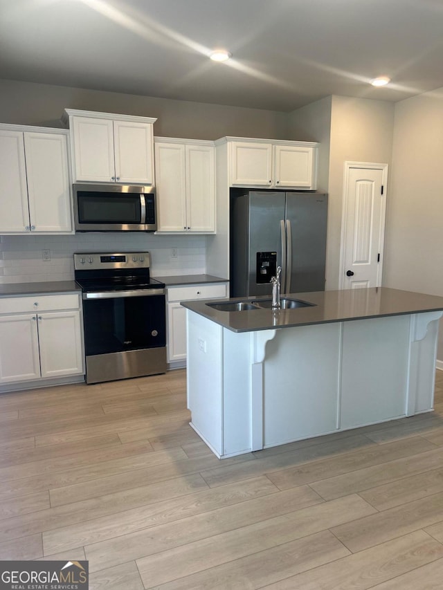 kitchen with appliances with stainless steel finishes, white cabinetry, a kitchen island with sink, and sink